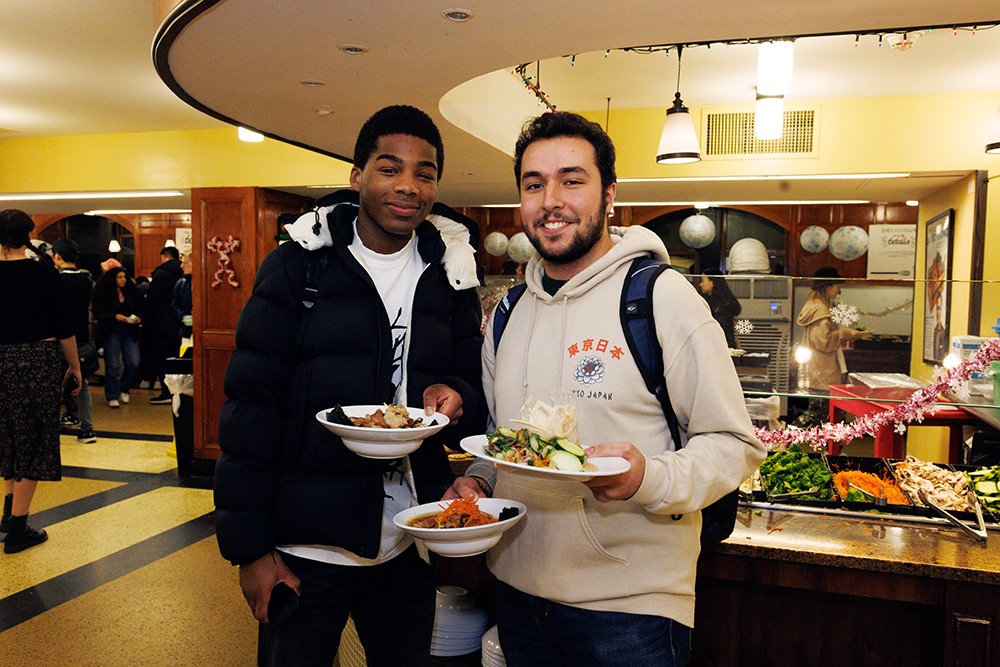 Two students stand in John Jay with plates of food