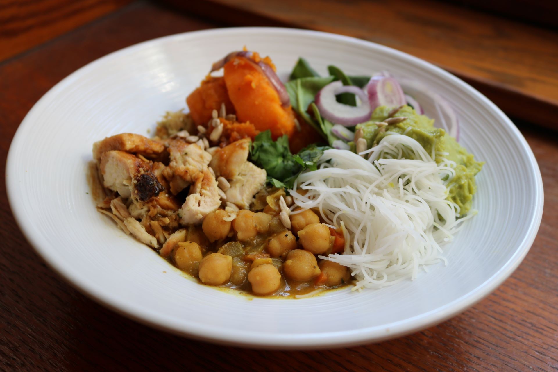 Thai sunbutter buddha bowl with chicken, chick peas, roasted sweet potato, rice noodles, avocado, spinach, and red onions.