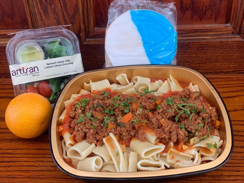 A typical meal prepared for students during the delivery period. (Photo: Campus Services) A pasta and meat sauce meal prepared for students during the delivery period, with a salad, orange, and large white and blue cookie.