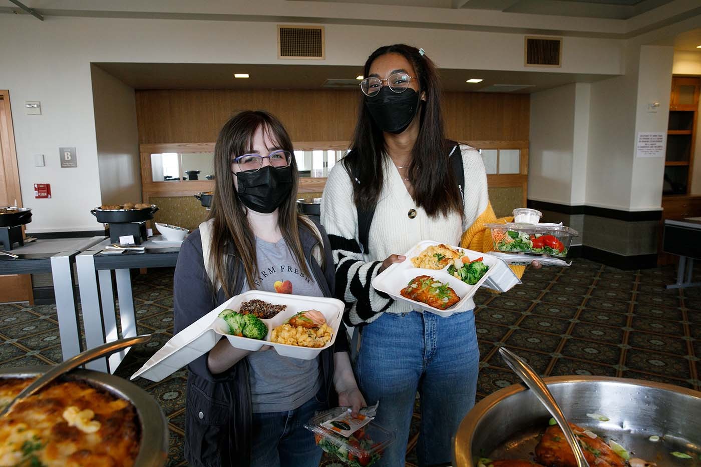 Mercy and Skylar standing in the serving line holding to-go containers full of food.