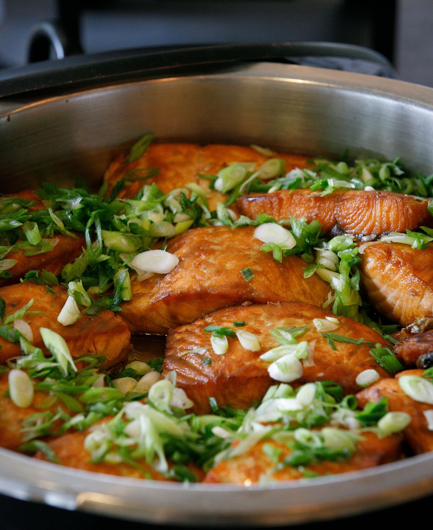 Salmon topped with green onion slices in a black serving dish