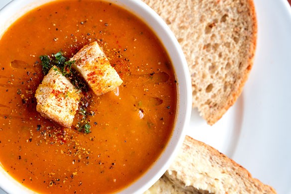 Close up of tomato soup with bread in white bowl and plate