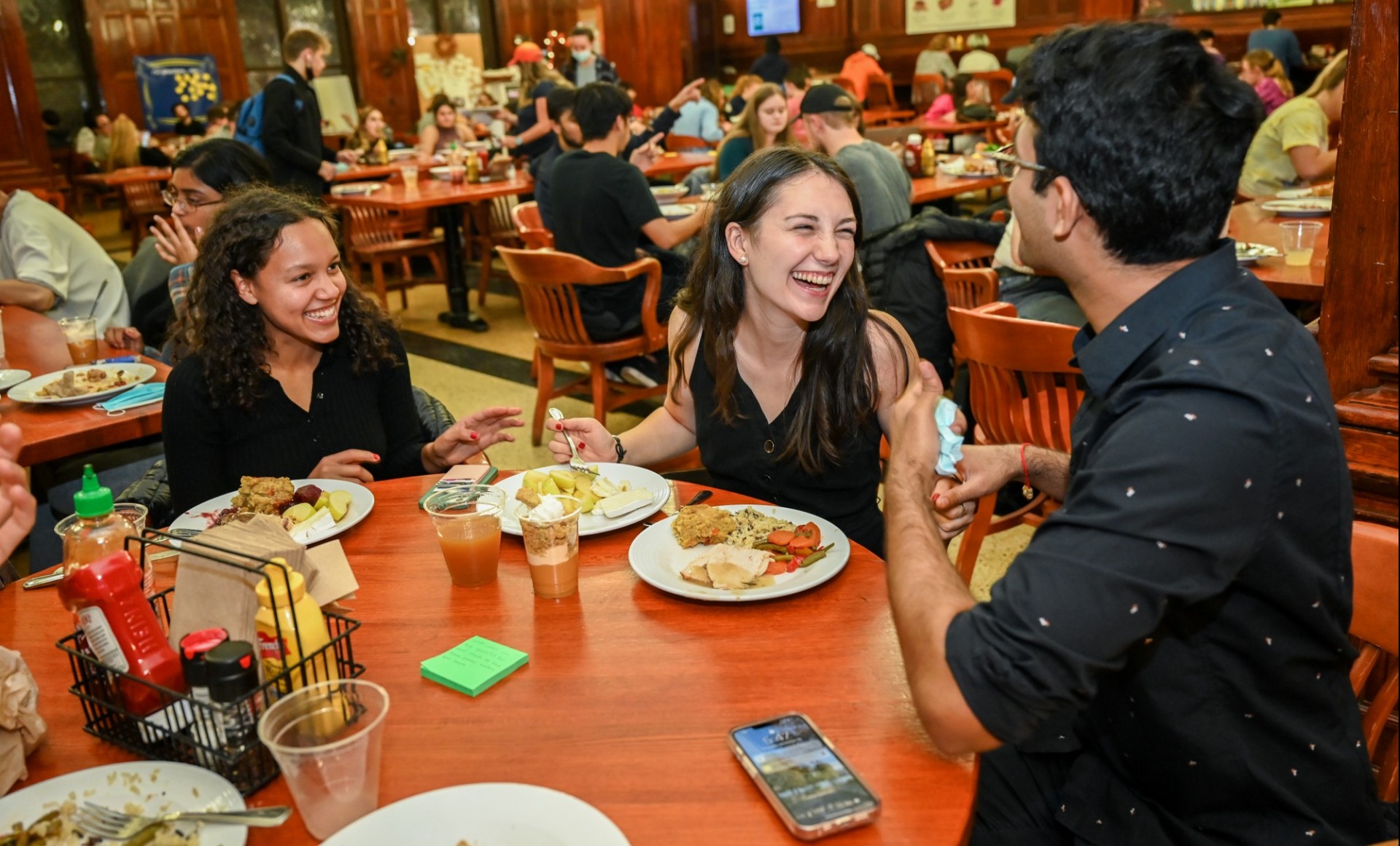 Three students laughing while eating in the dining hall