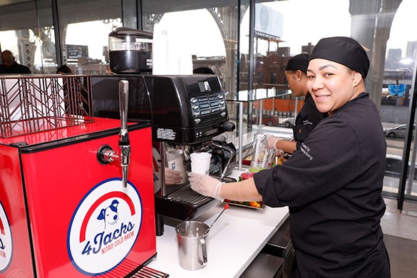 Columbia Dining staff smiling into the camera and preparing coffee. Additional Columbia dining staff member in the background