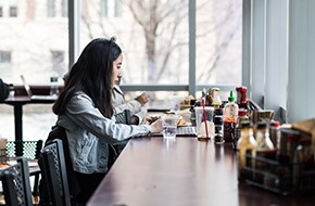 Student sitting alone eating while working on her laptop