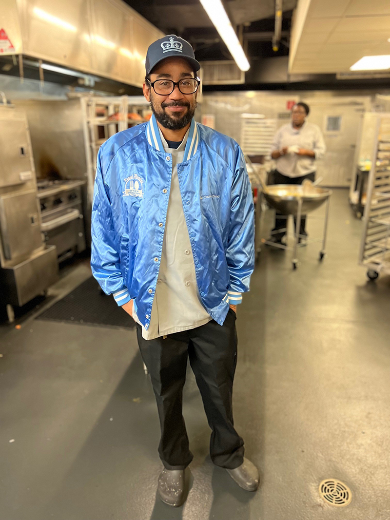 John Jay team member Damien models the blue bomber jacket in the John Jay kitchen