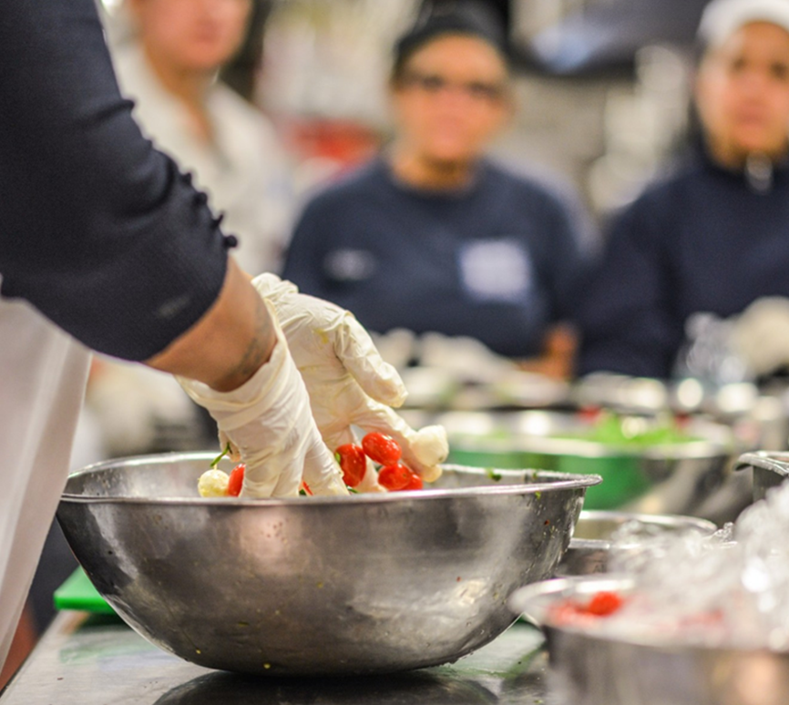 Chef hand-mixing mozzarella balls and tomatoes in stainless steel bowl