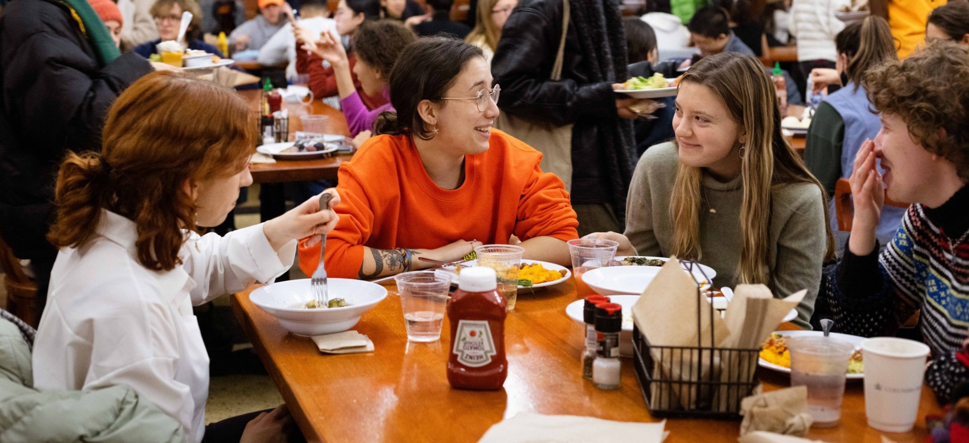 Four students laughing while eating in the dining hall