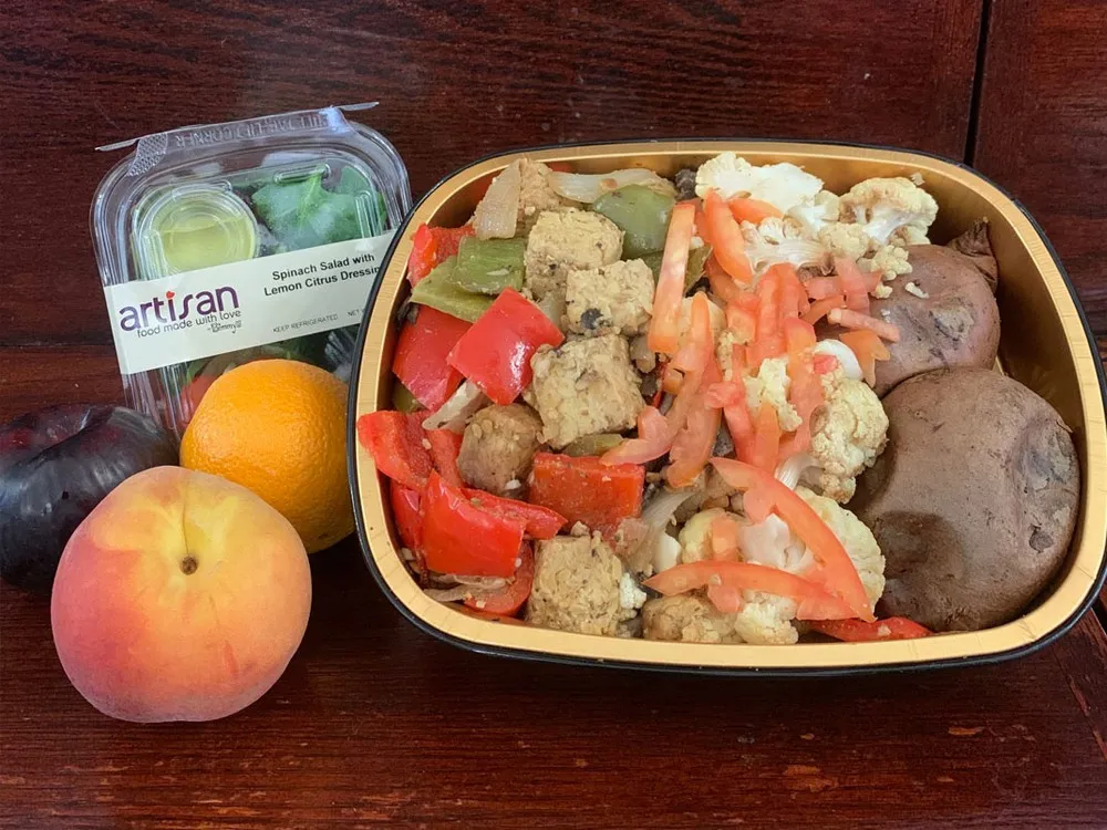 A vegetarian/vegan meal prepared for students during the delivery period including a salad, a plum, peach, and orange.