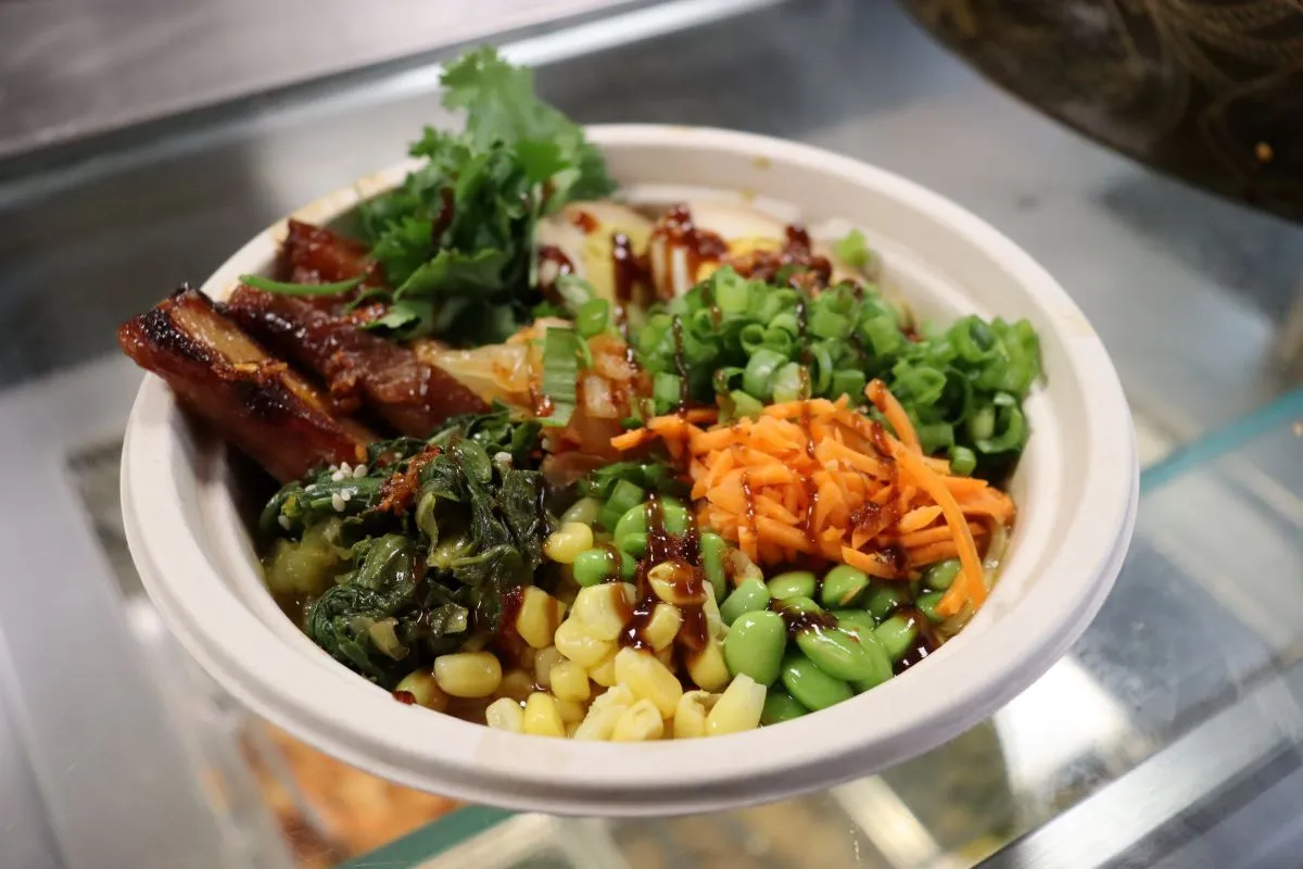 A bowl of ramen topped with pork belly, carrots, edamame, bok choy, and green onions
