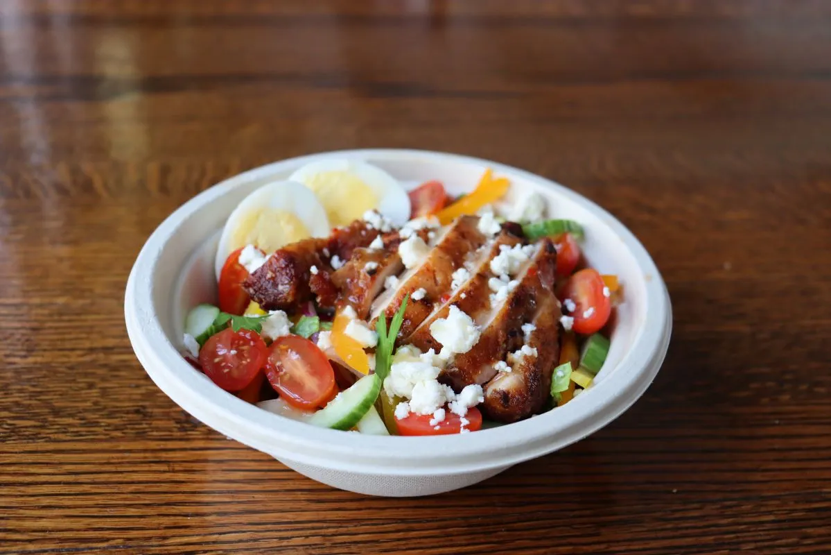 A bowl of salad topped with glazed chicken, feta, and grape tomatoes