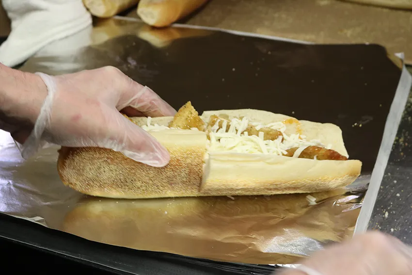 A sub shop worker is holding one end of the hot honey chicken sub